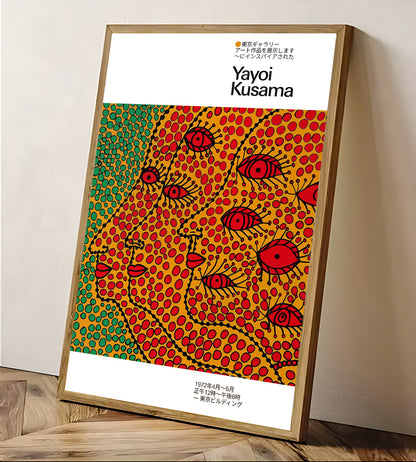 Framed art poster inspired by Yayoi Kusama featuring colorful dotted abstract faces in red, yellow, and green, leaning against a wall on a wooden floor.