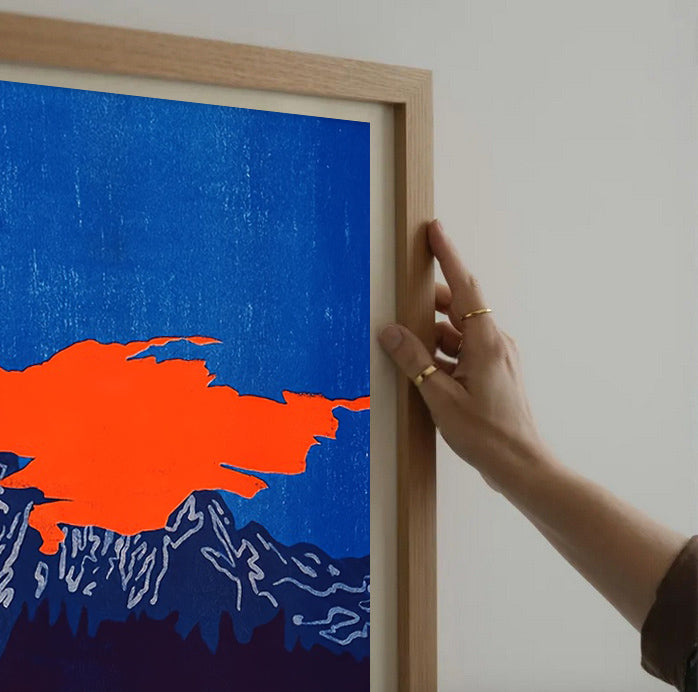 Person holding a framed artwork with an orange abstract shape on a blue background