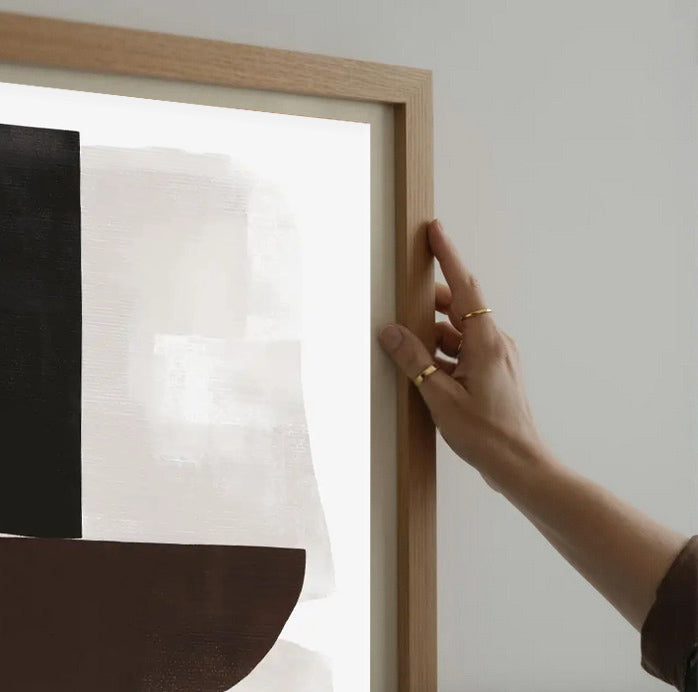 Person adjusting a wooden picture frame on a wall.