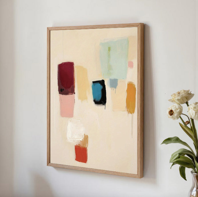 Framed abstract art with colorful blocks on a wall next to a vase of flowers.