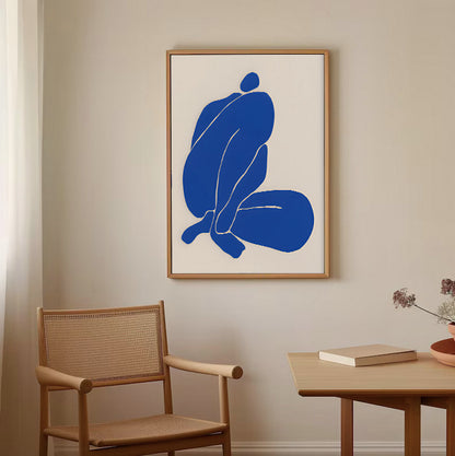 Framed abstract art with blue shapes on a beige wall above a wooden chair and table.