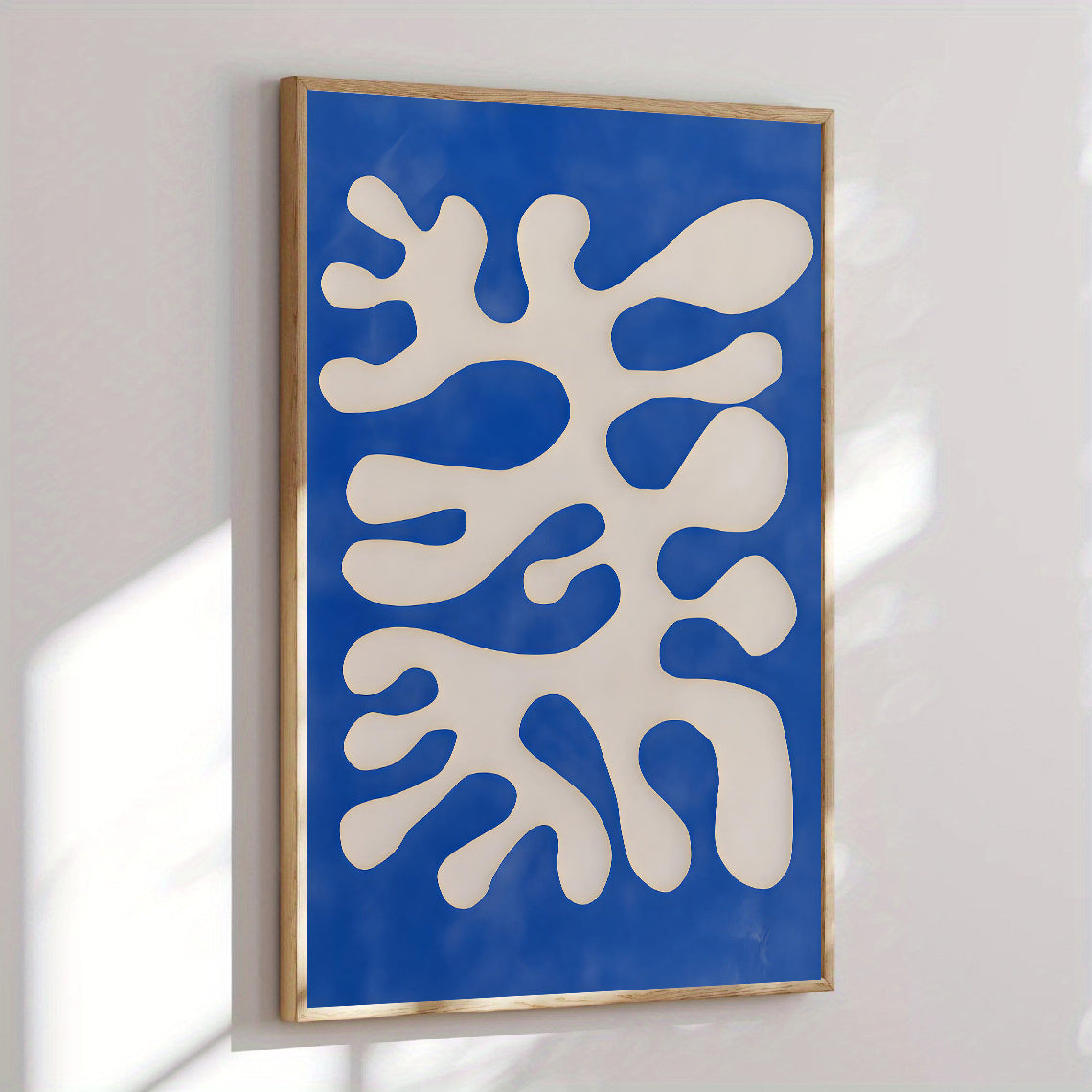 Abstract art piece with white shapes on a blue background in a wooden frame.