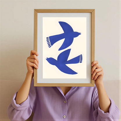 Person holding a framed artwork with blue birds on a beige background