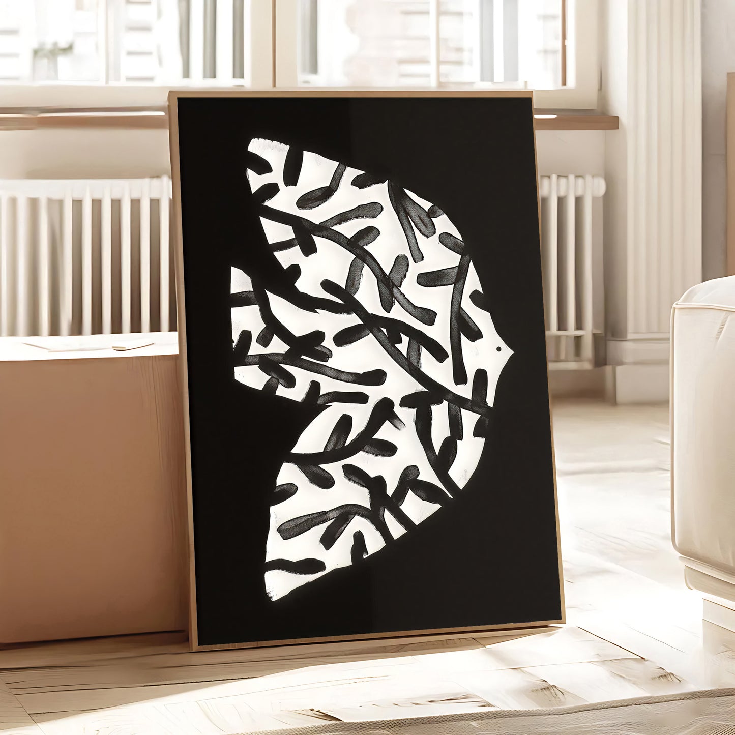 Framed abstract art piece with black and white design on a wooden floor.