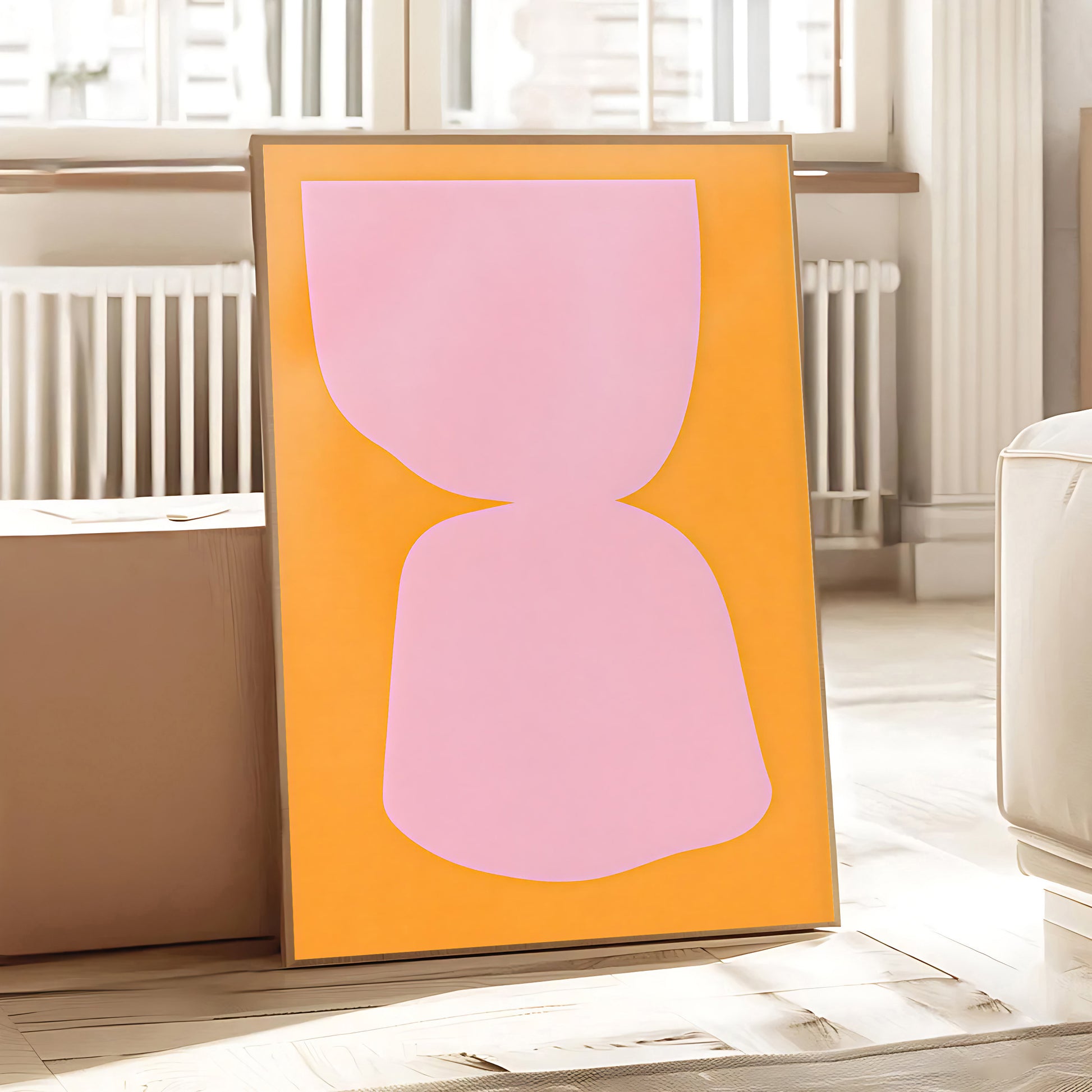 Framed abstract artwork with a pink shape on an orange background in a room.