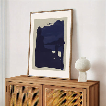 Framed abstract art piece on a wooden cabinet with a white vase.