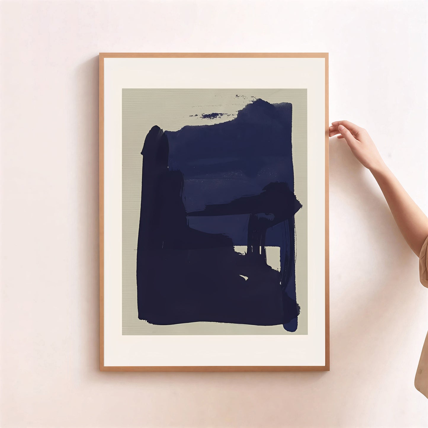 Framed abstract art print with a large blue shape on a beige background, held by a person.