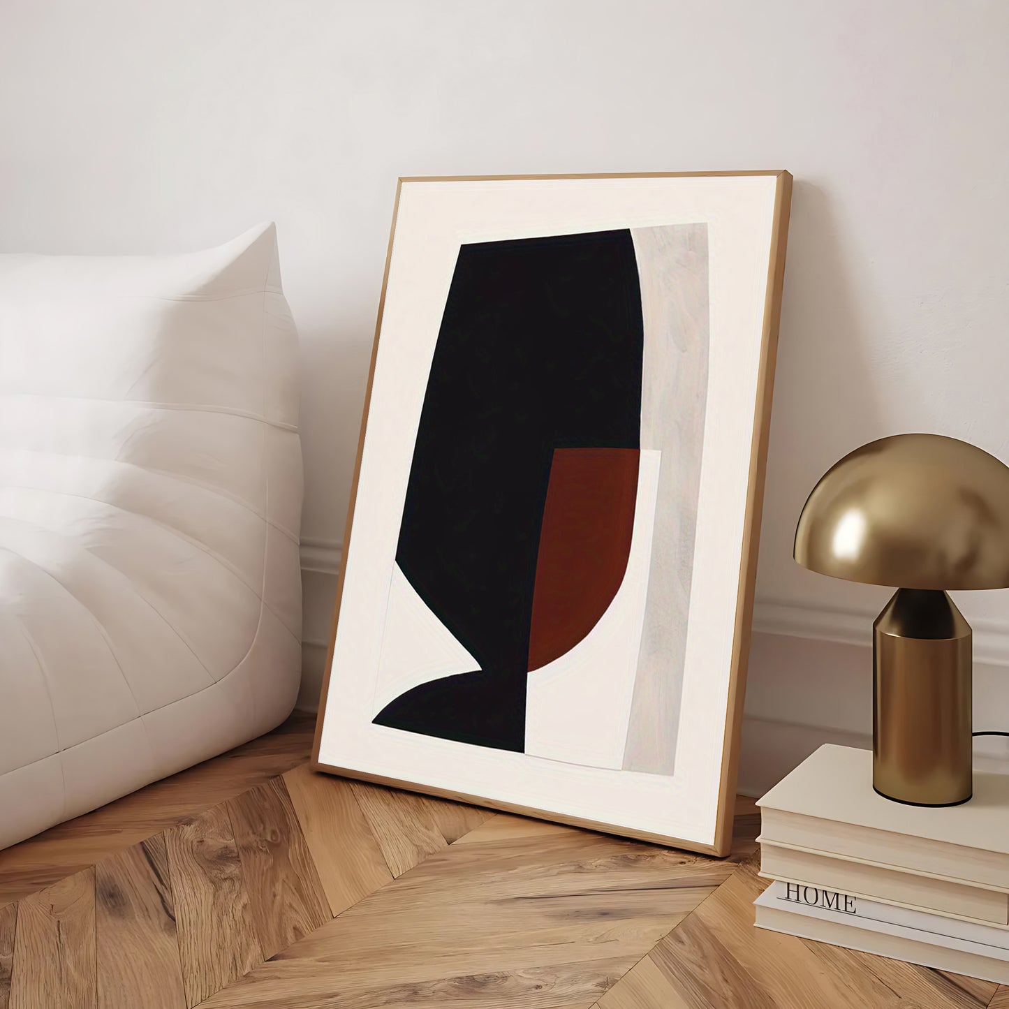 Framed abstract art piece on a wooden floor with a lamp and books in the background.