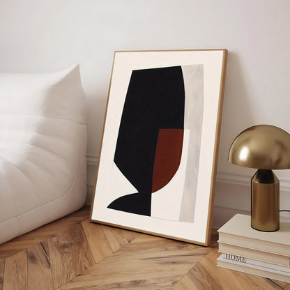 Framed abstract art piece on a wooden floor with a lamp and books in the background.