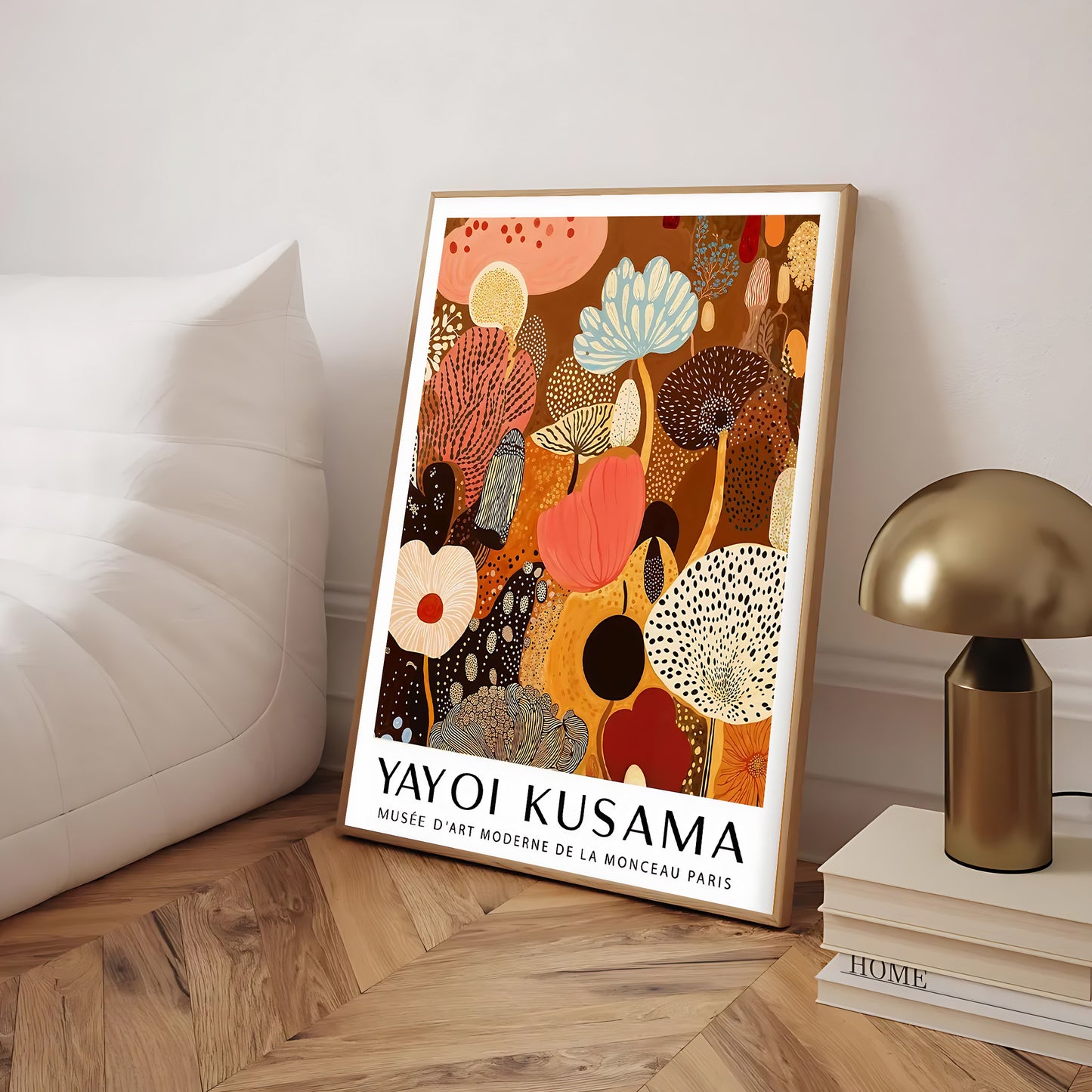 Framed Yayoi Kusama artwork on a wooden floor with a lamp and books in the background