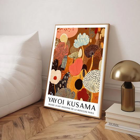 Framed Yayoi Kusama artwork on a wooden floor with a lamp and books in the background