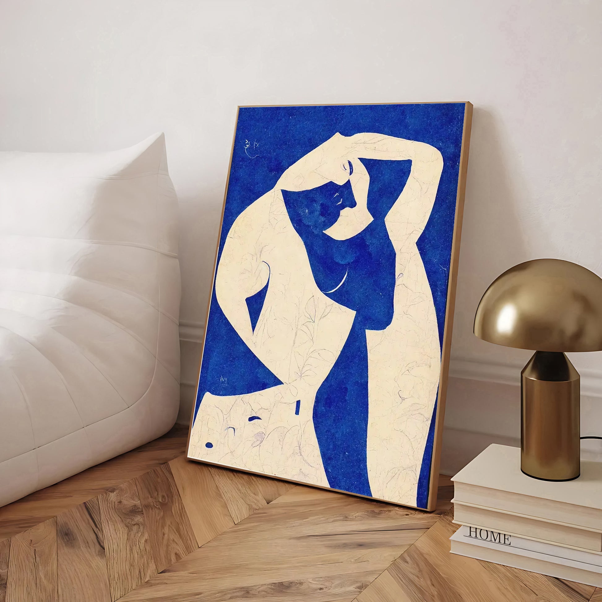 Abstract artwork of a nude figure on a blue background in a room with a lamp and books.