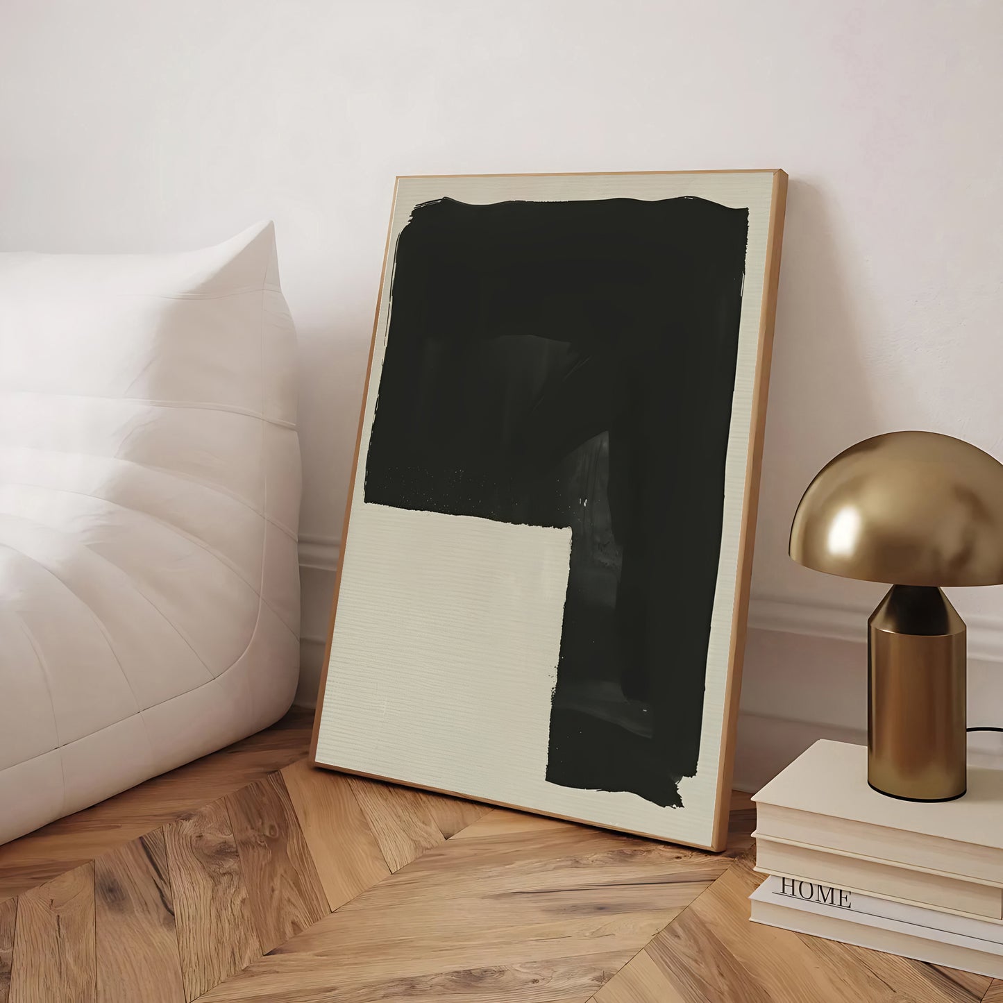 Framed abstract art piece on a wooden floor with a lamp and books in the background.
