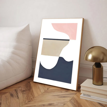Abstract art print in a wooden frame on a wooden floor with a lamp and books in the background.