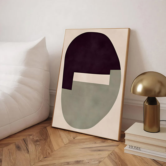 Abstract art piece on a wall next to a gold lamp and books on a wooden floor.