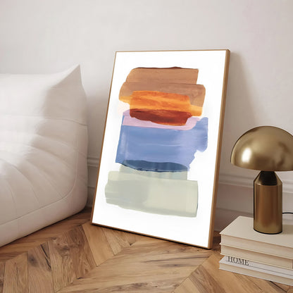 Abstract art print in a wooden frame on a wooden floor with a lamp and books in the background.