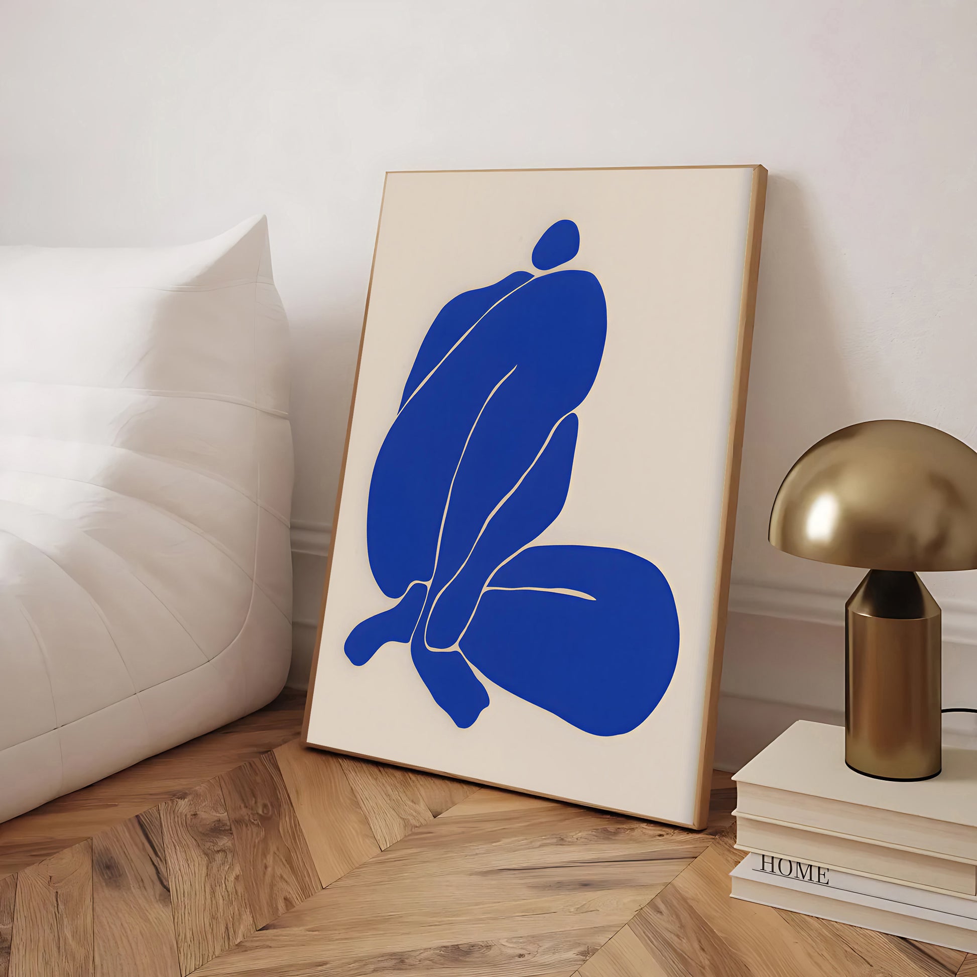 Abstract art print with blue shapes on a beige background, placed on a wooden floor.