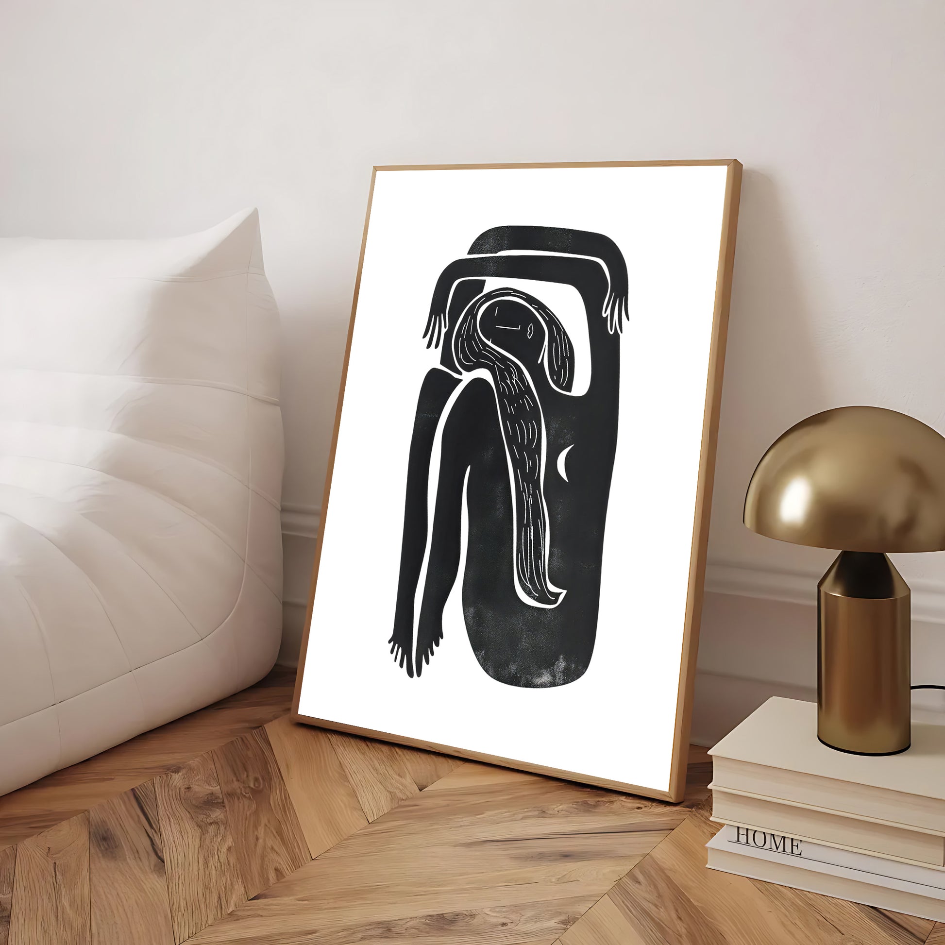 Framed black and white abstract artwork on a wooden floor with a lamp and books in the background.