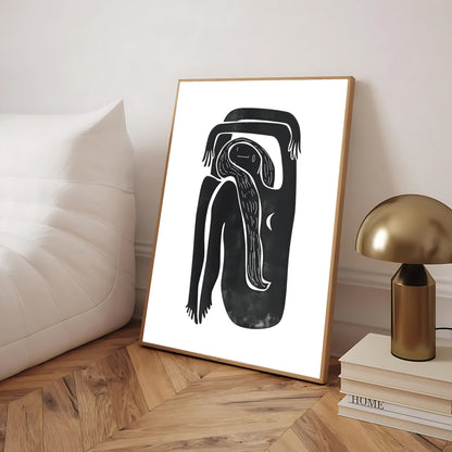 Framed black and white abstract artwork on a wooden floor with a lamp and books in the background.