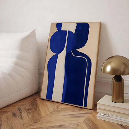 Abstract art piece with blue and beige design on a wooden floor, next to a gold lamp and books.