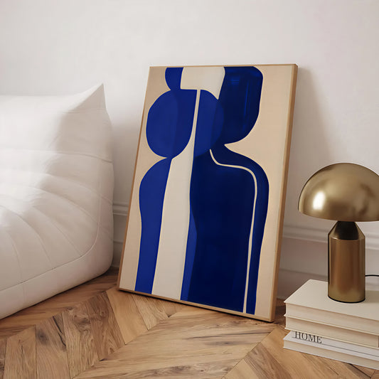 Abstract art piece with blue and beige design on a wooden floor, next to a gold lamp and books.