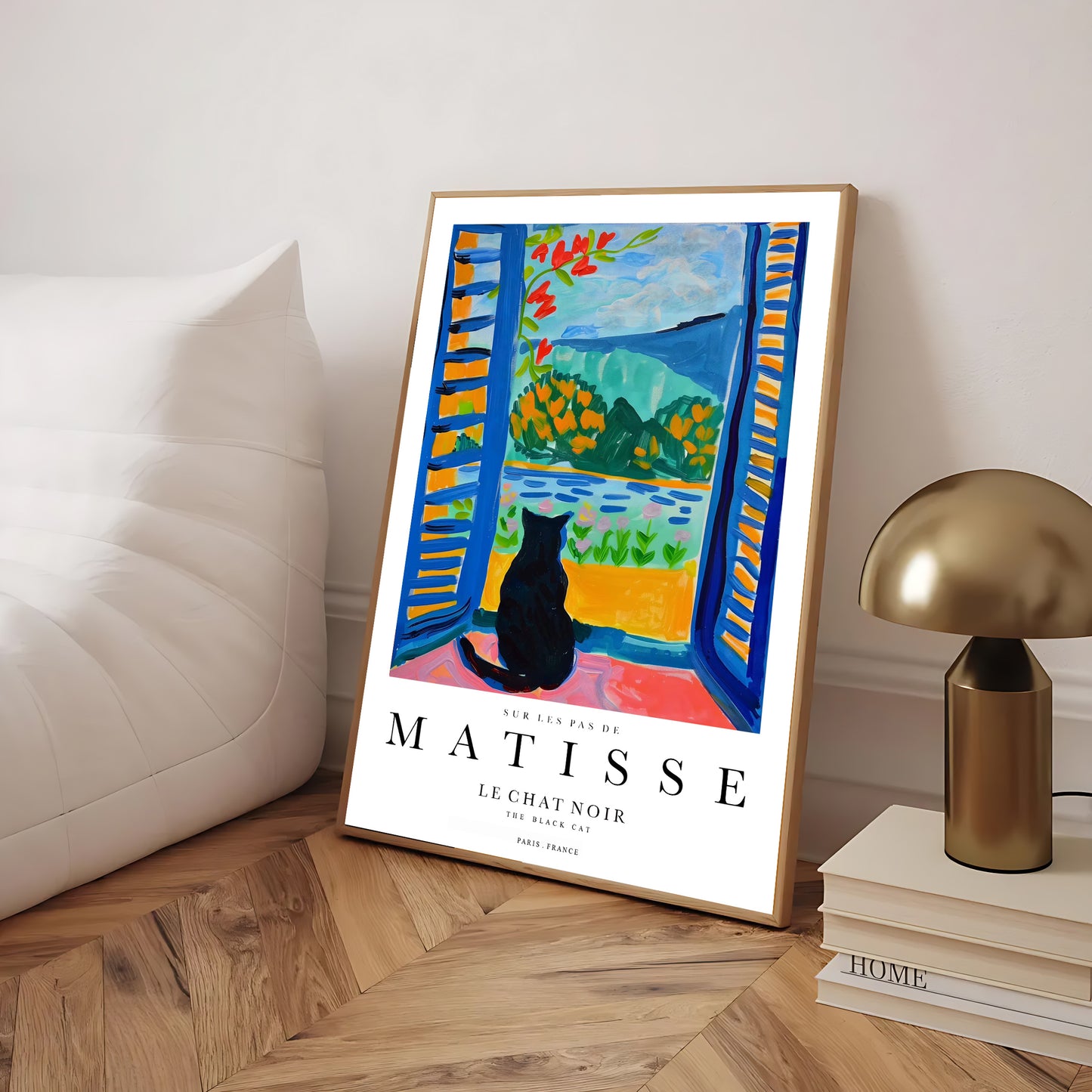 Framed Matisse art print with a black cat by a lamp and books on a wooden floor.