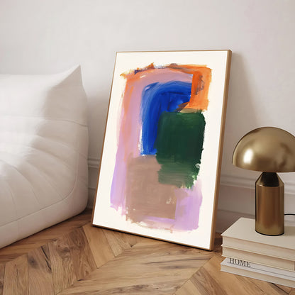 Framed abstract art piece on a wooden floor with a lamp and books in the background.