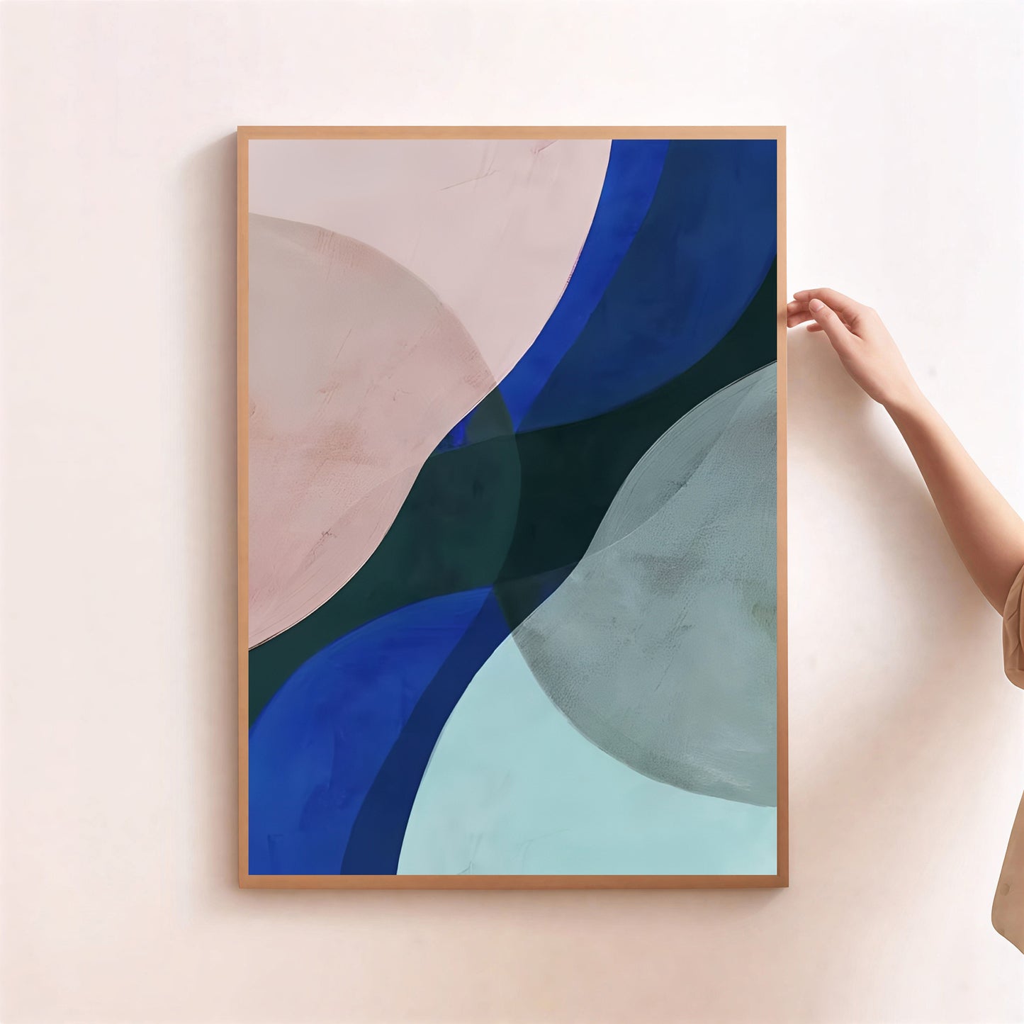 Abstract art print with blue and green shapes in a wooden frame on a light pink wall.