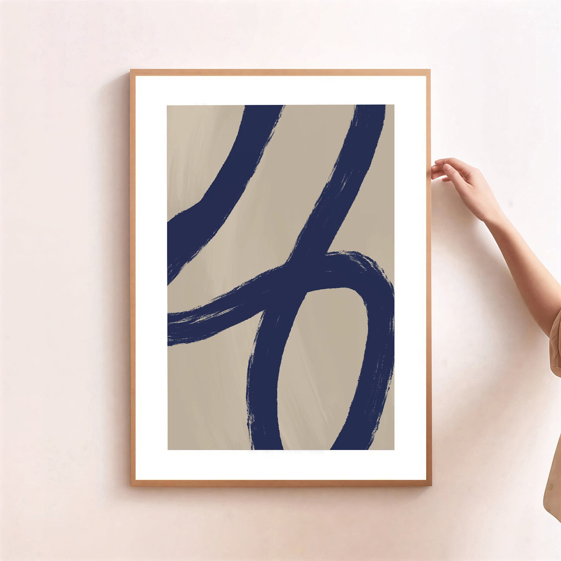 Framed abstract art print with blue strokes on a beige background, held by a person.