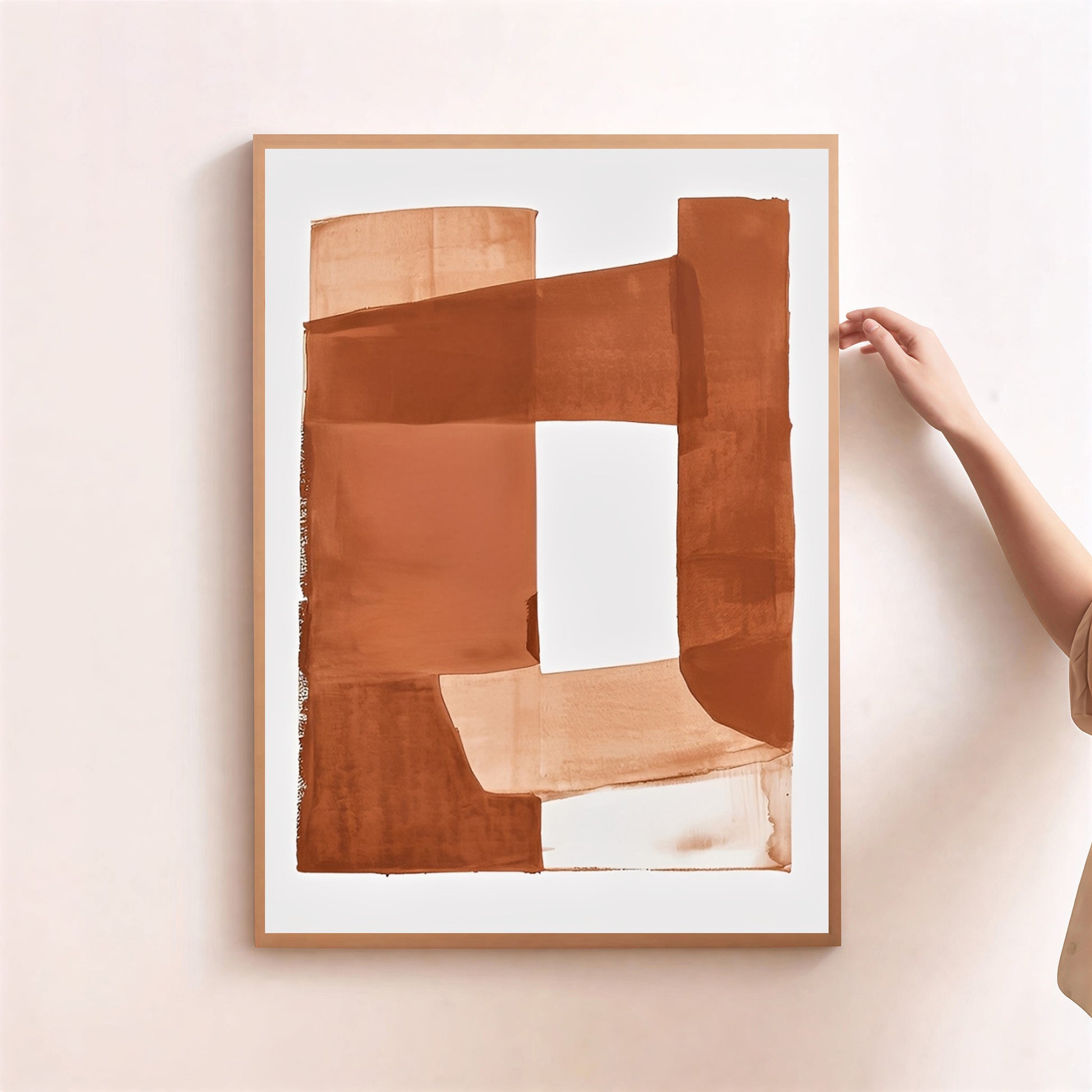 Framed abstract art piece with brown and beige colors on a light pink wall.