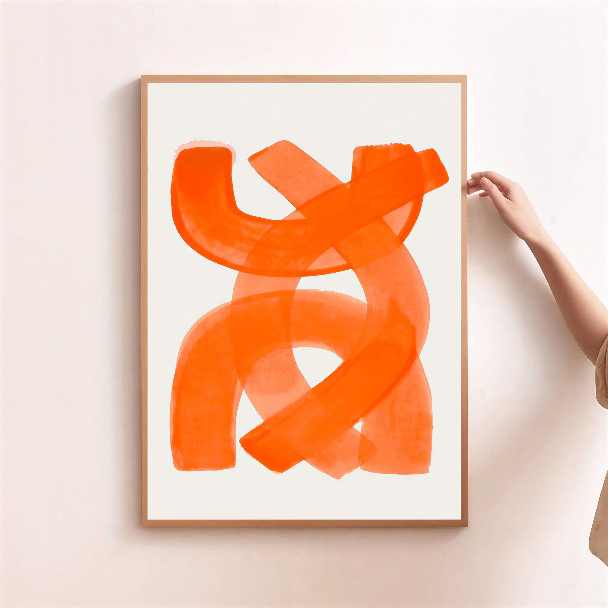 Framed abstract orange artwork on a white wall with a hand adjusting the frame.