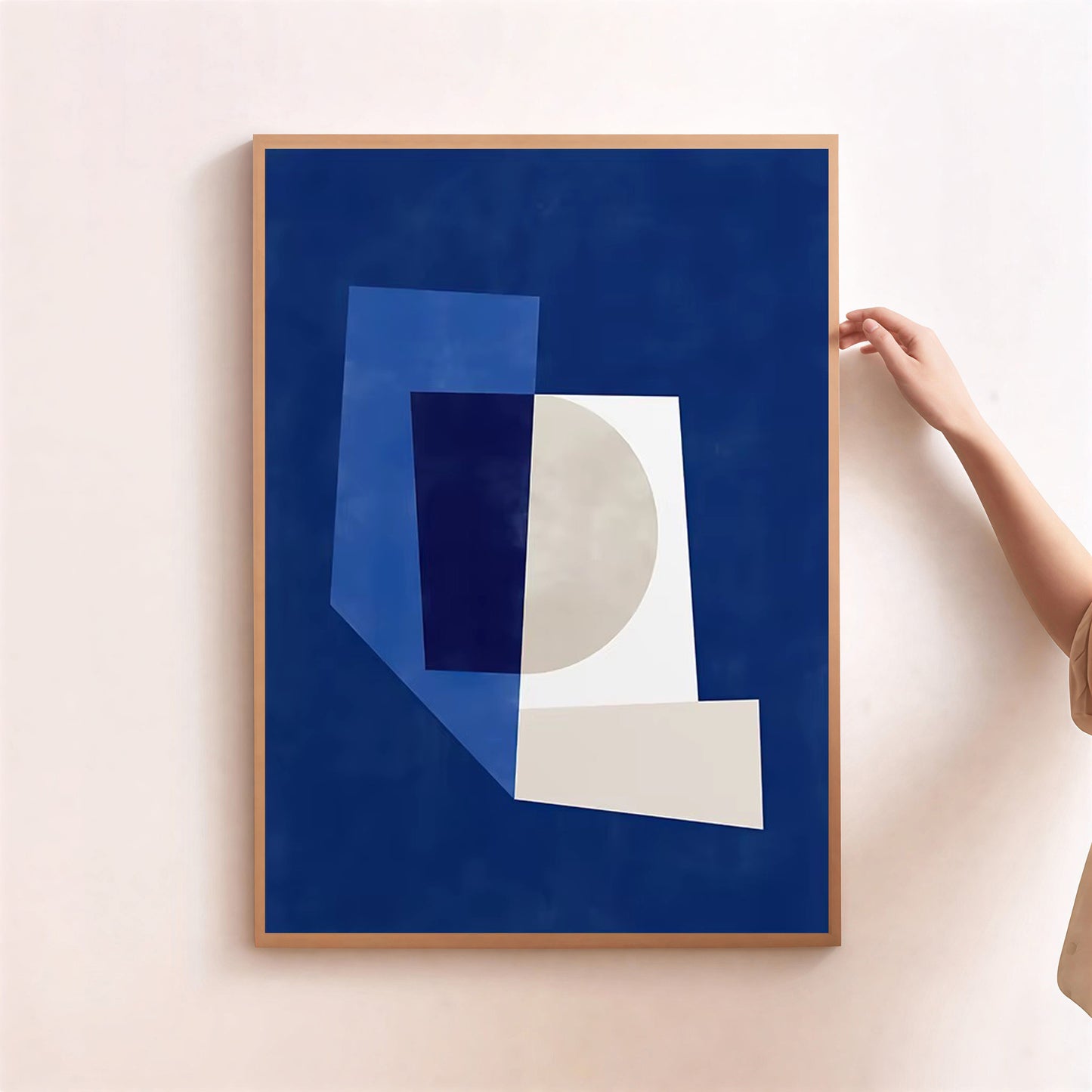 Framed abstract art print with geometric shapes on a blue background, held by a person against a light pink wall.