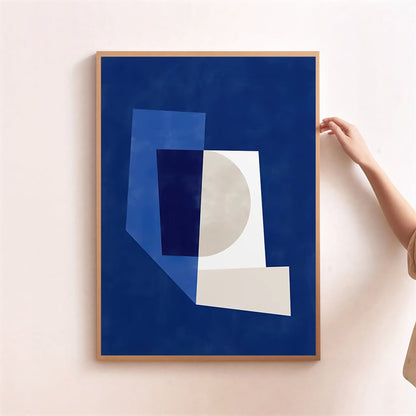 Framed abstract art print with geometric shapes on a blue background, held by a person against a light pink wall.