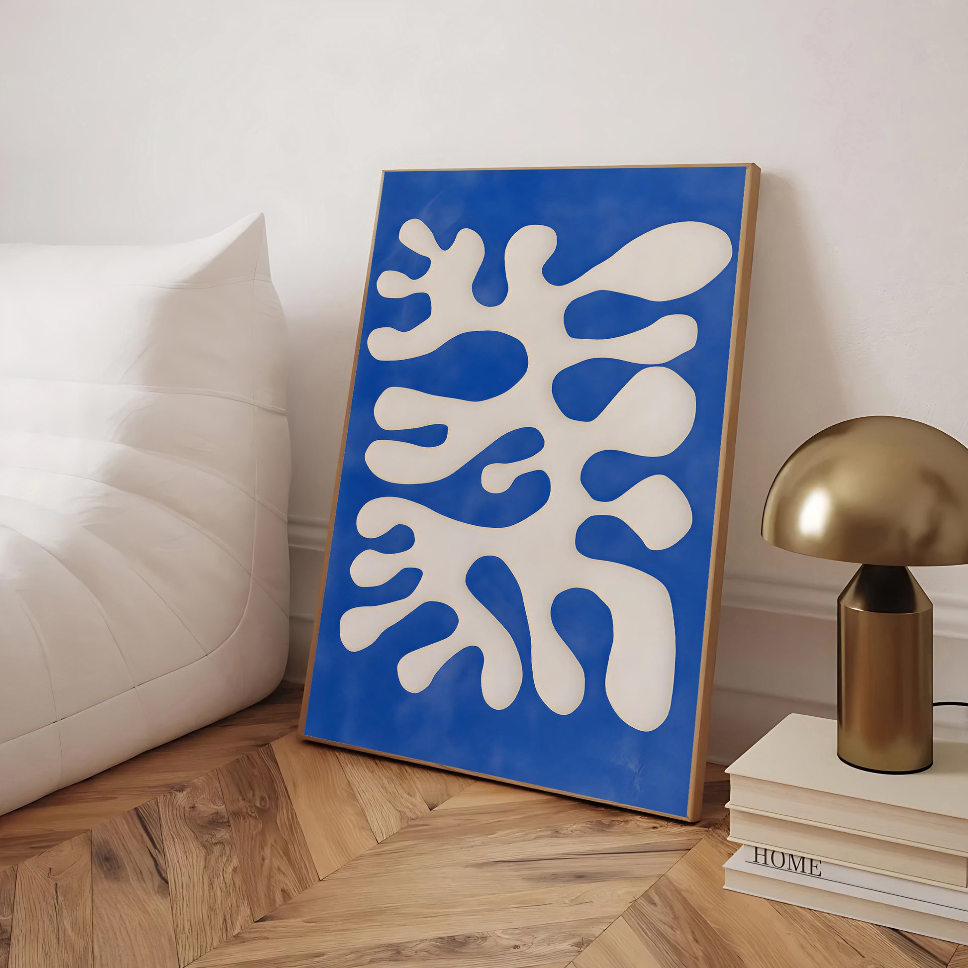 Blue and white abstract art piece on a wooden floor with a gold lamp and books in the background.