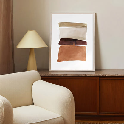 Framed abstract art on a wall above a wooden cabinet with a lamp and beige armchair.