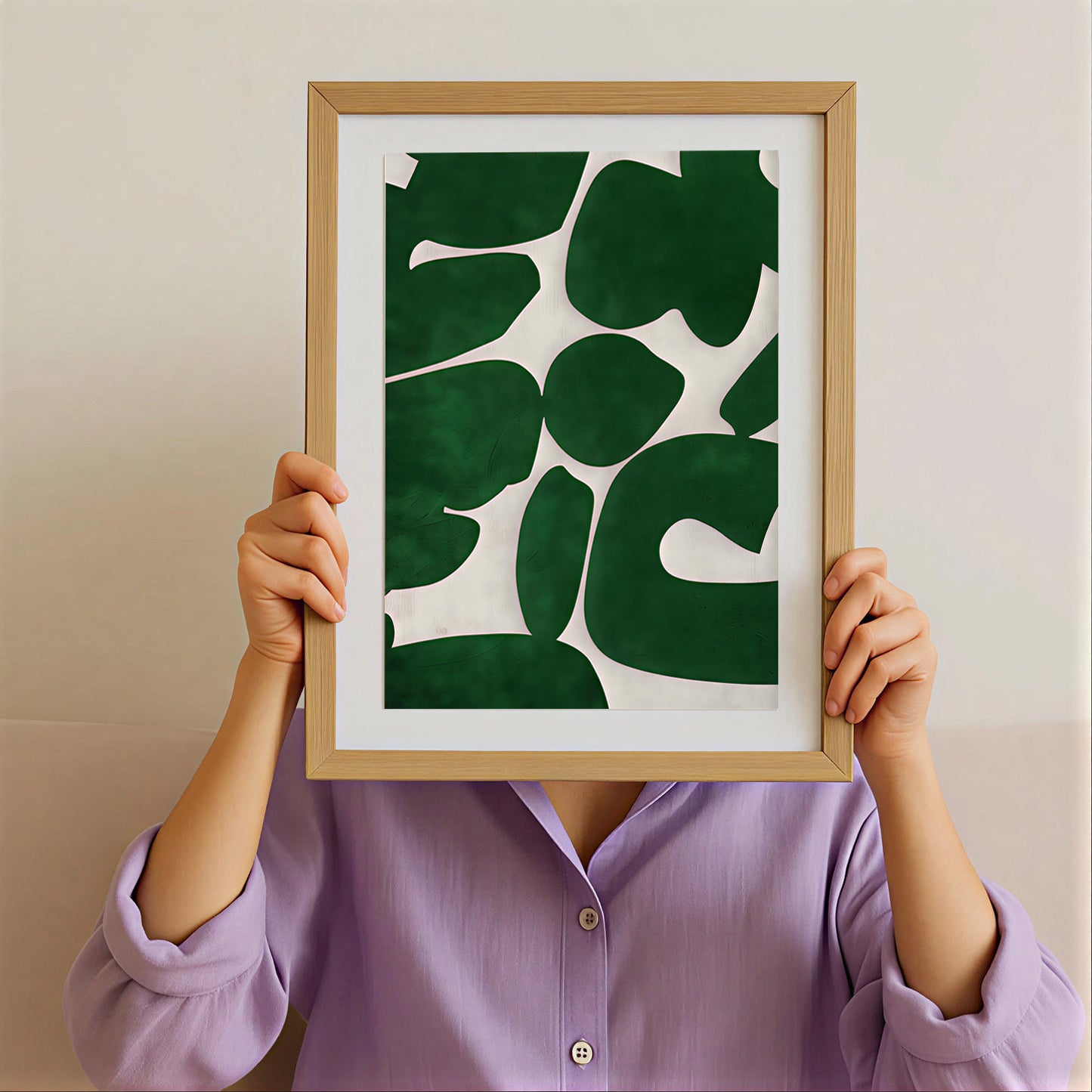 Person holding a framed green leaf pattern poster against their face on a plain background