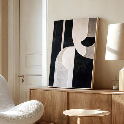 Abstract black and white painting on a wooden shelf in a room with a white chair and lamp.
