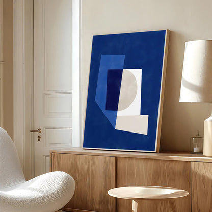 Abstract blue and white artwork on a wooden shelf in a room with a white chair and lamp.
