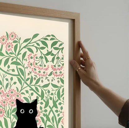 Hand holding a framed artwork with floral design and black cat silhouette.
