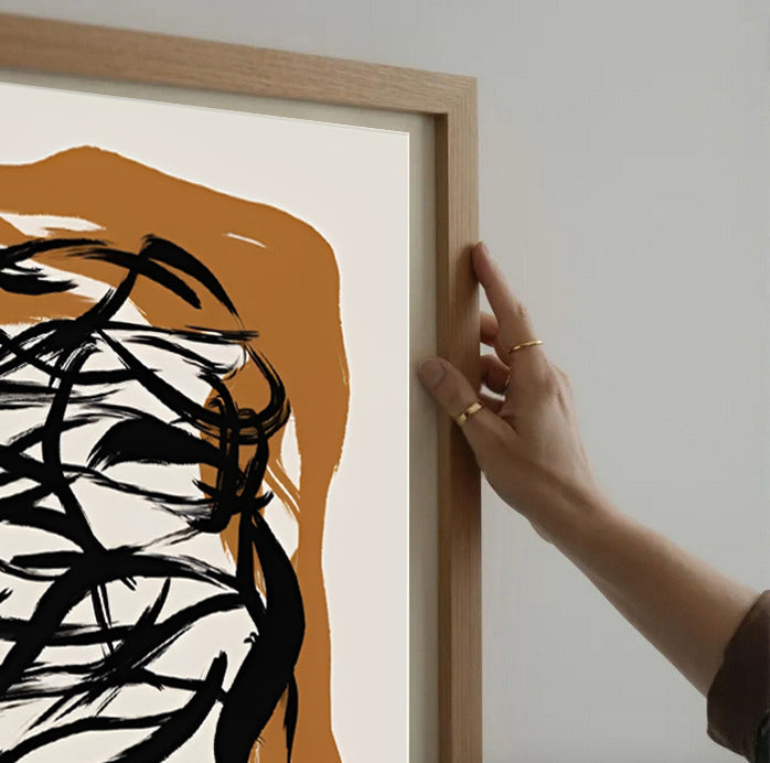 Person adjusting a wooden frame on an abstract artwork with black and orange design.