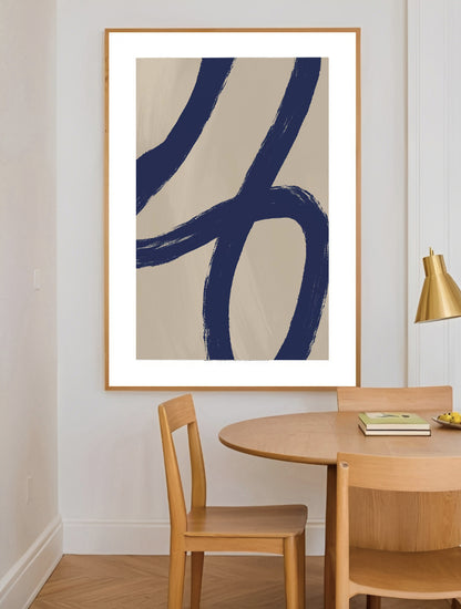 Abstract art piece with blue brush strokes in a gold frame above a wooden dining table.